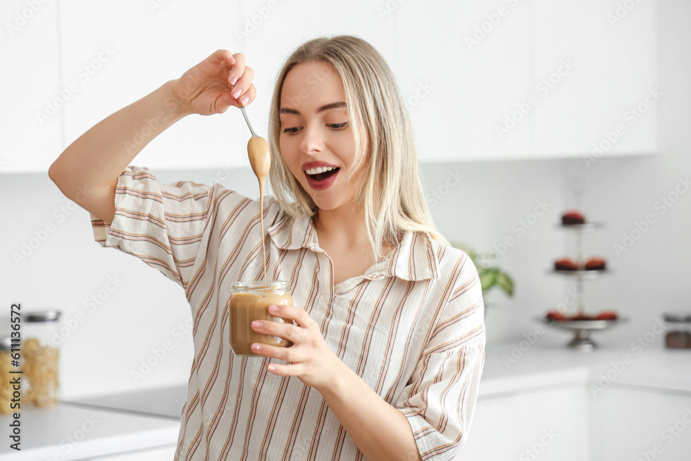 Young woman with spoon and jar of nut butter in kitchen