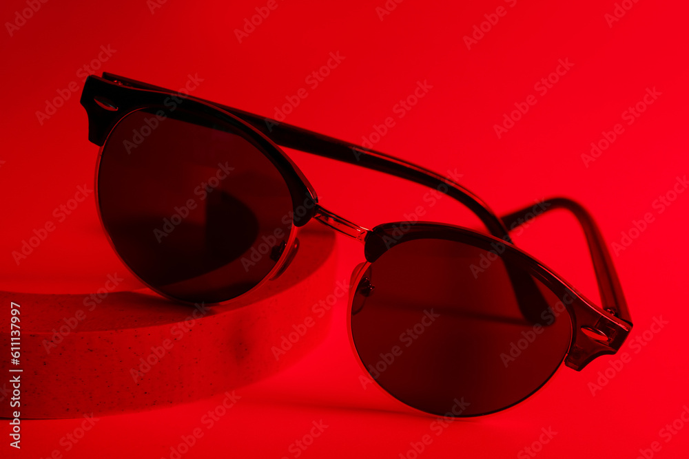 Podium with stylish sunglasses on red background