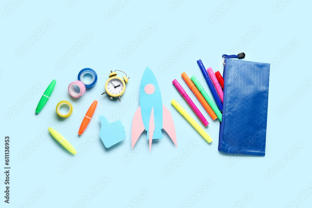 Paper rocket with pencil case and different stationery on blue background