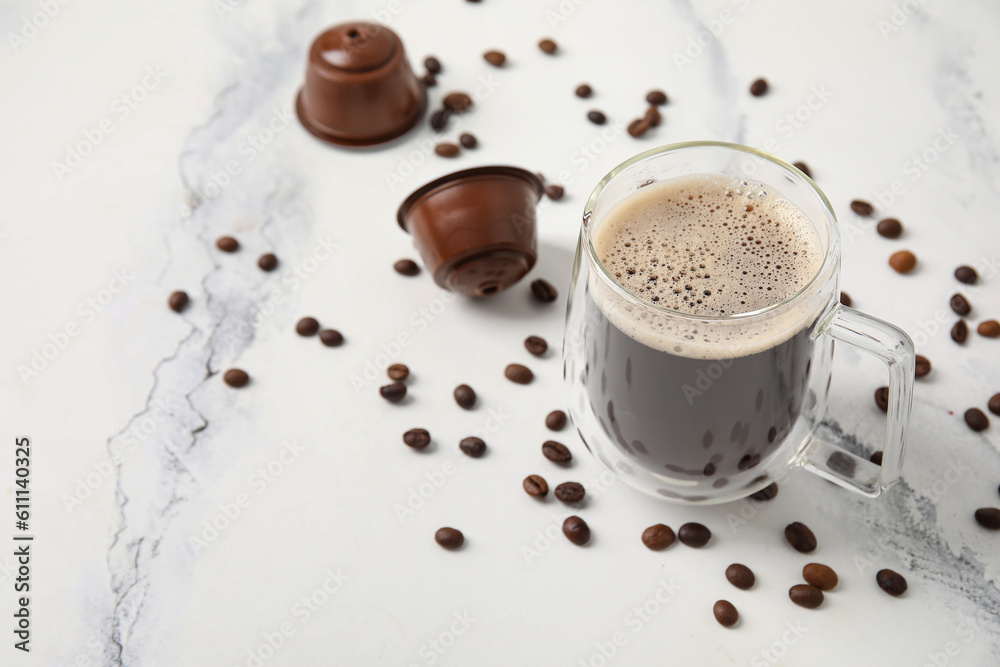 Cup of delicious coffee, pods and beans on white table