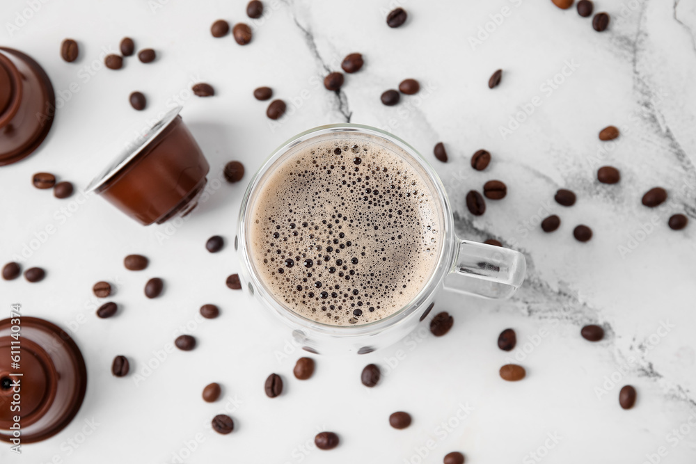 Cup of delicious coffee, pods and beans on white table