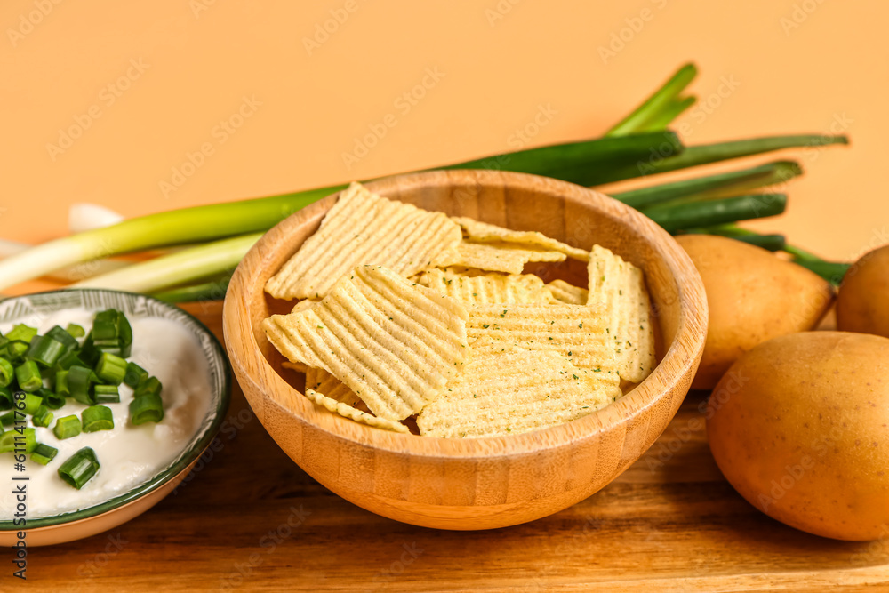 Bowl of tasty sour cream with sliced green onion and potato chips on orange background