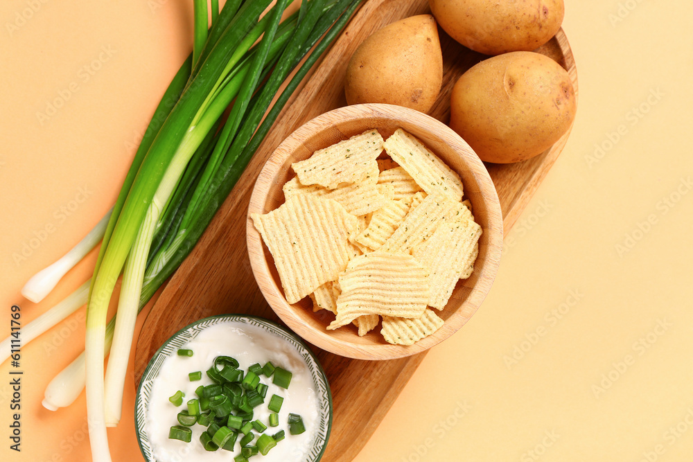 Bowl of tasty sour cream with sliced green onion and potato chips on orange background