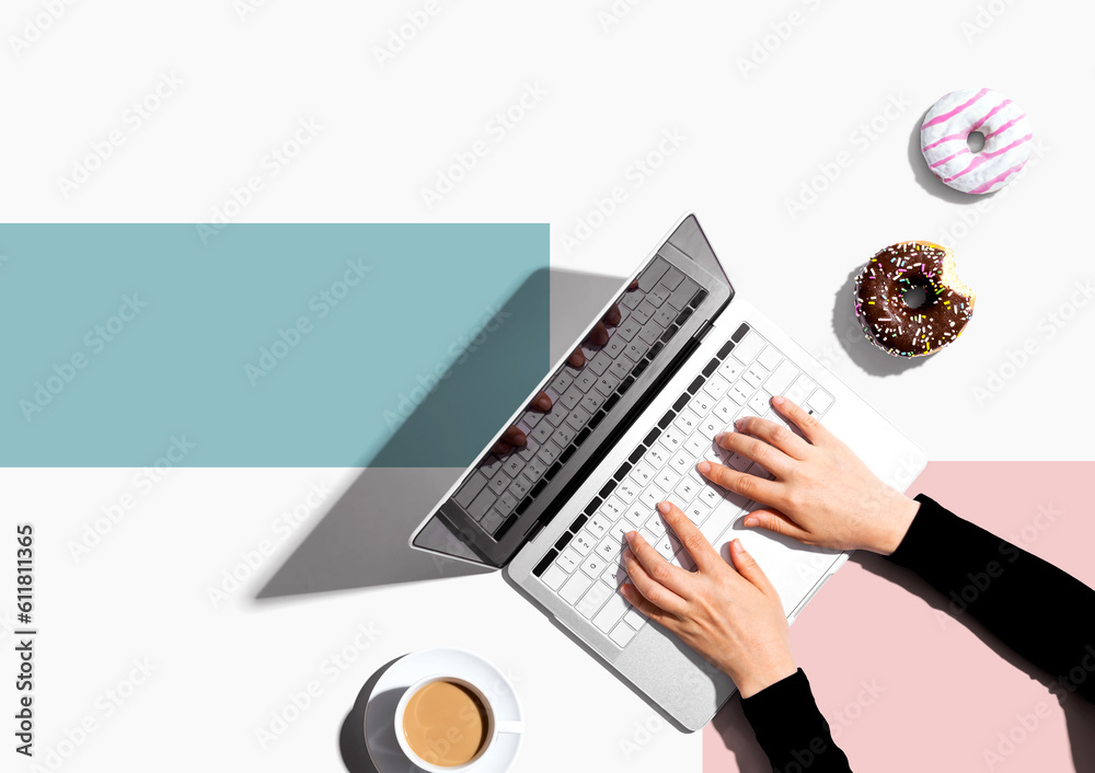 Person using a laptop computer with a donut and a cup of coffee - Flat lay