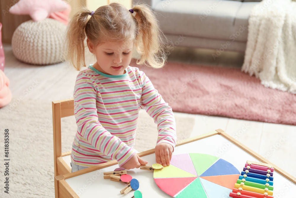 Cute little girl playing matching game with clothespins at home