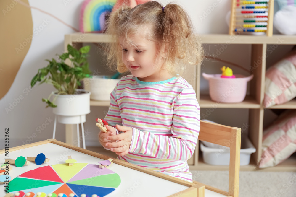 Cute little girl playing matching game with clothespins at home