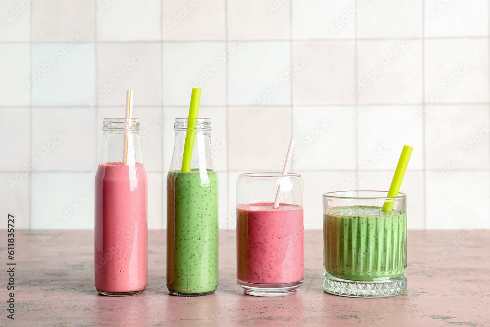 Glasses and bottles of colorful smoothie on pink table