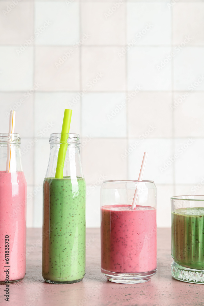 Glasses and bottles of colorful smoothie on pink table