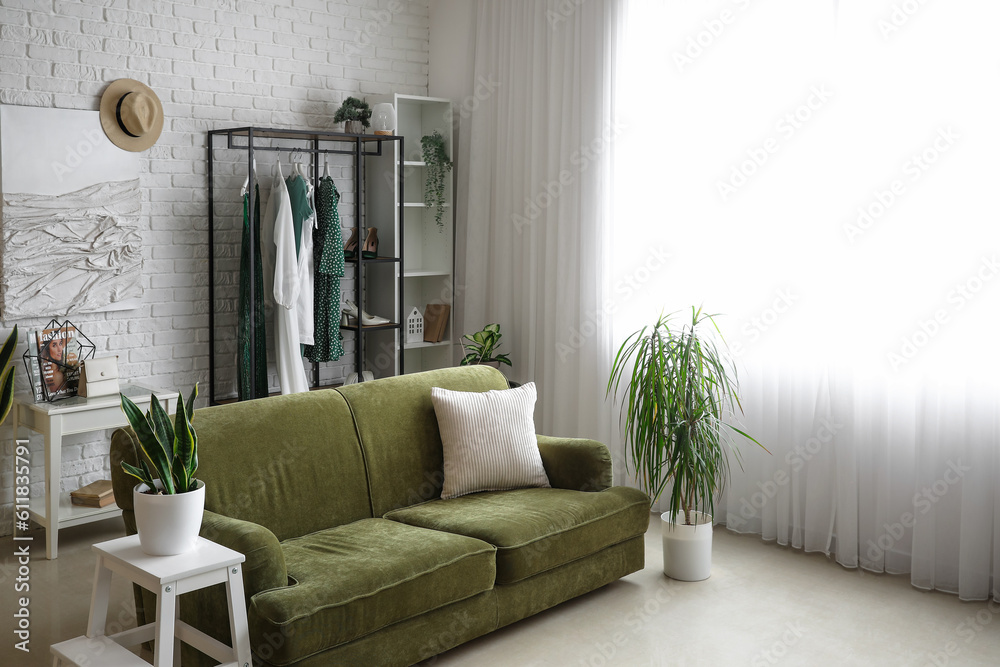 Interior of light room with sofa, shelving unit and clothes