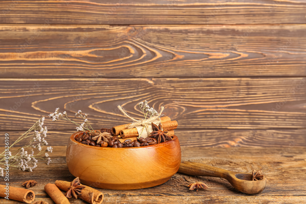 Bowl of coffee beans, cinnamon sticks and dried flowers on wooden background