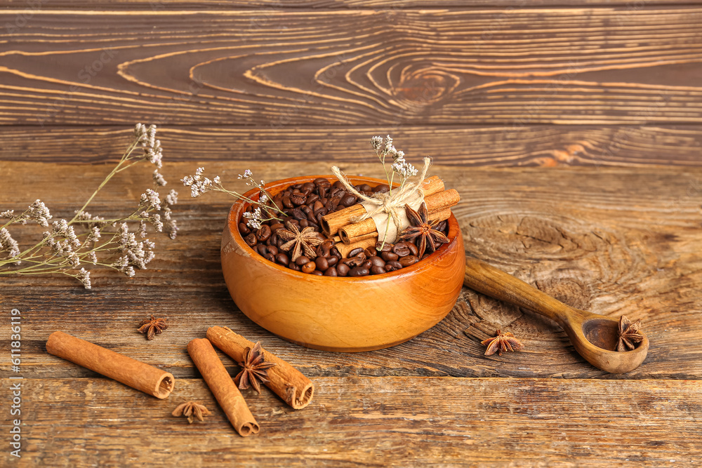 Bowl of coffee beans, cinnamon sticks and dried flowers on wooden background