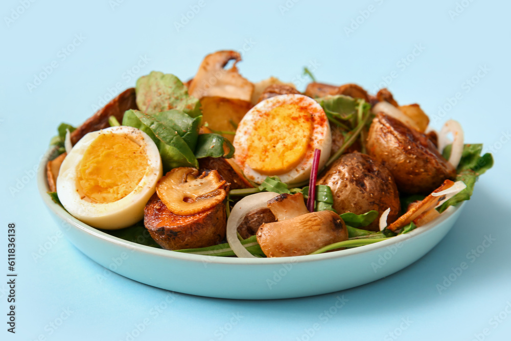 Plate of tasty potato salad with eggs and mushrooms on light blue background