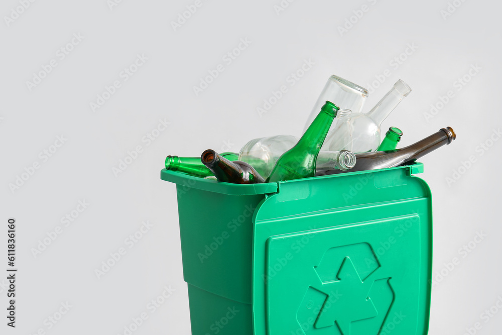 Container for garbage with glass bottles on light background. Recycling concept