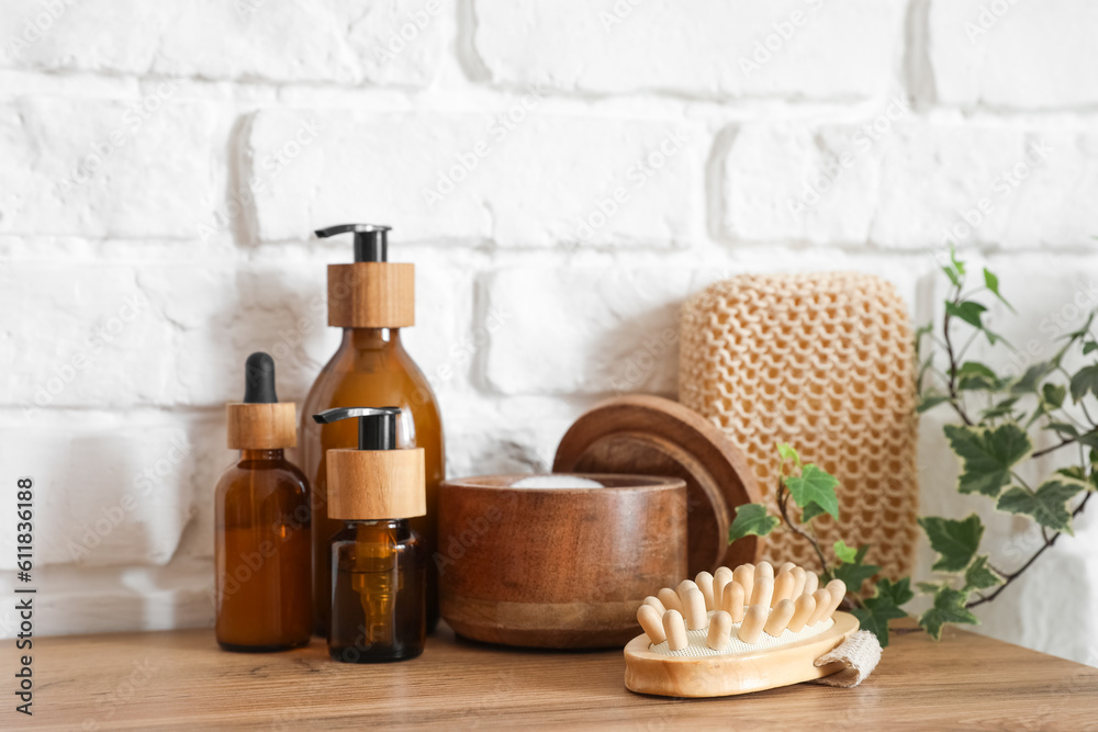 Bath accessories with massage brush on table near white brick wall