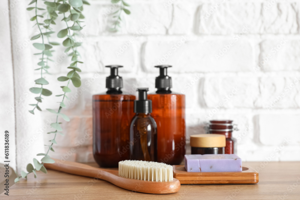 Bath accessories with massage brush on table near white brick wall