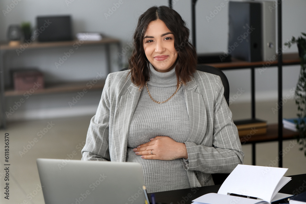 Young pregnant woman working at table in office