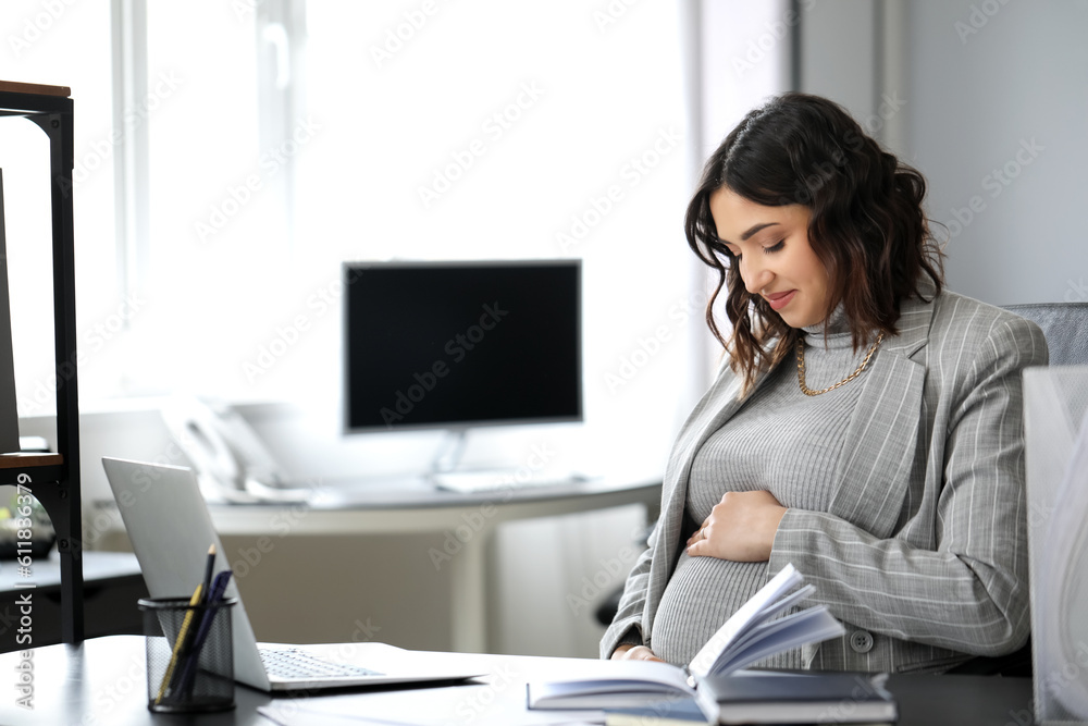 Young pregnant woman working at table in office