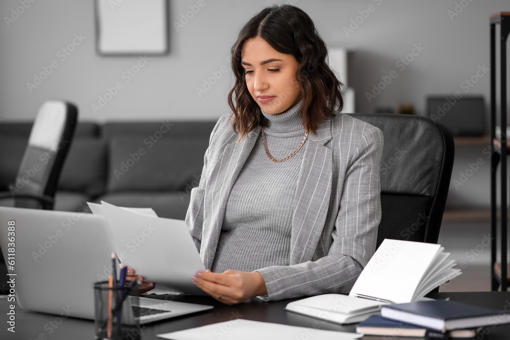 Young pregnant woman working with documents at table in office