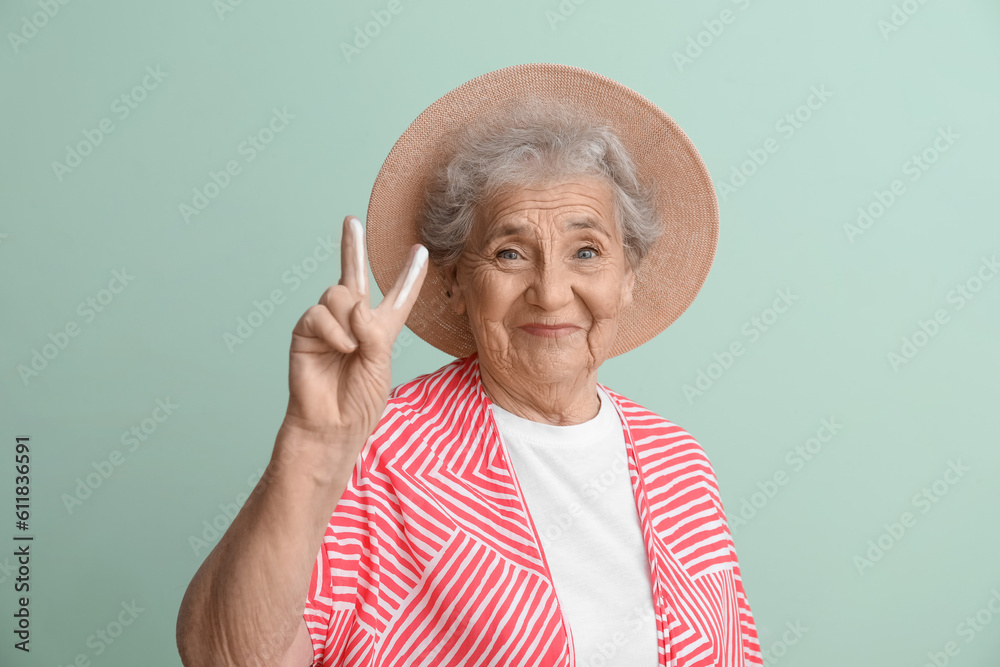 Senior woman with sunscreen cream showing victory gesture on green background