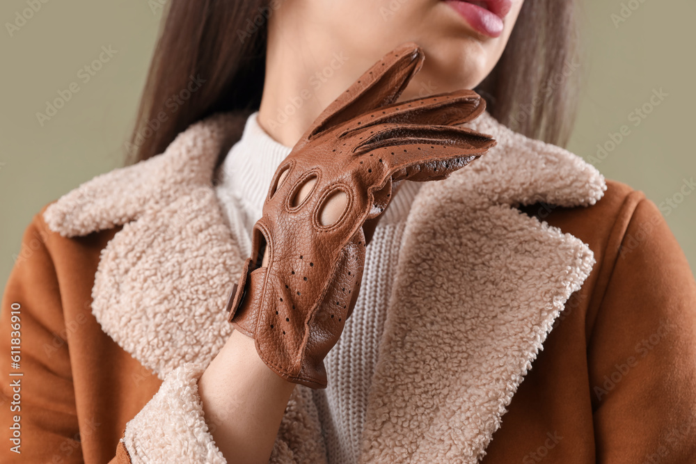 Stylish young woman in leather gloves on green background, closeup