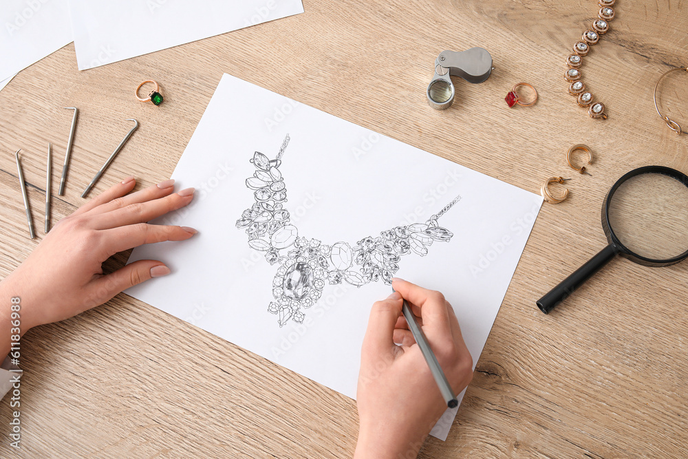 Female jeweler drawing adornment on wooden table, closeup