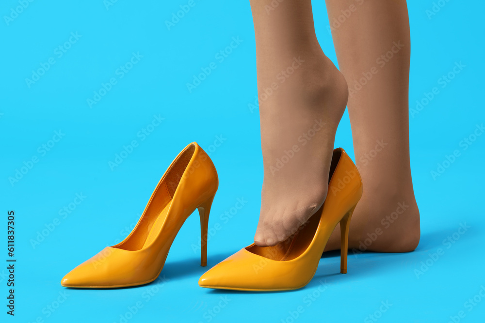 Female legs in tights with stylish high heels on color background, closeup