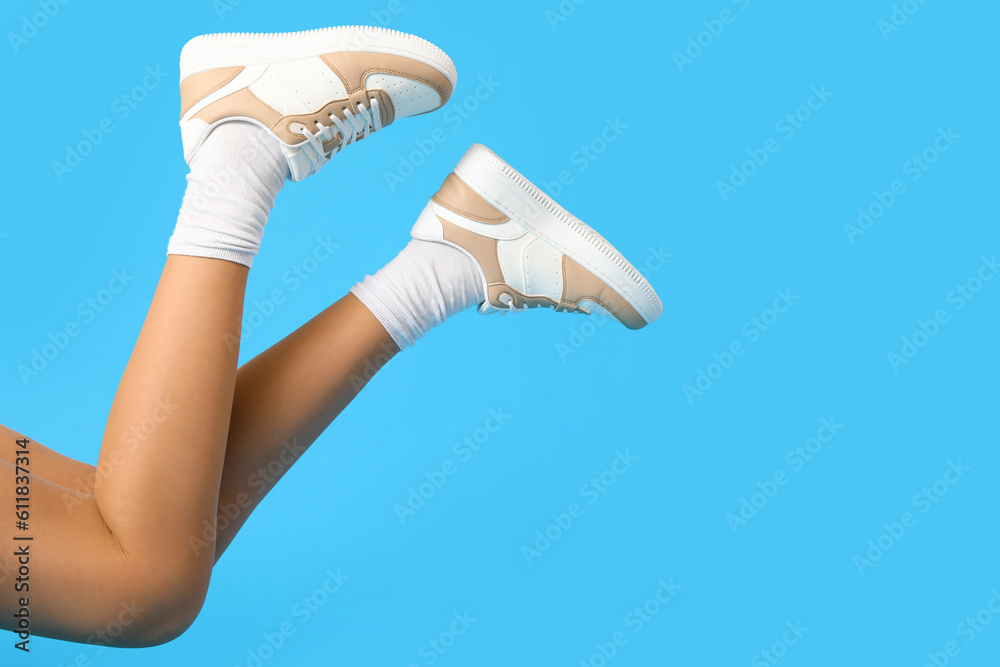 Female legs in stylish sneakers on color background, closeup