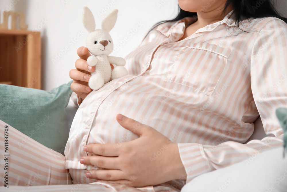 Young pregnant woman with toy sitting in bedroom, closeup