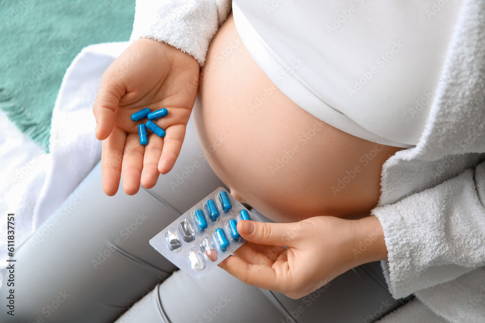 Pregnant woman with Folic Acid pills in bedroom, closeup