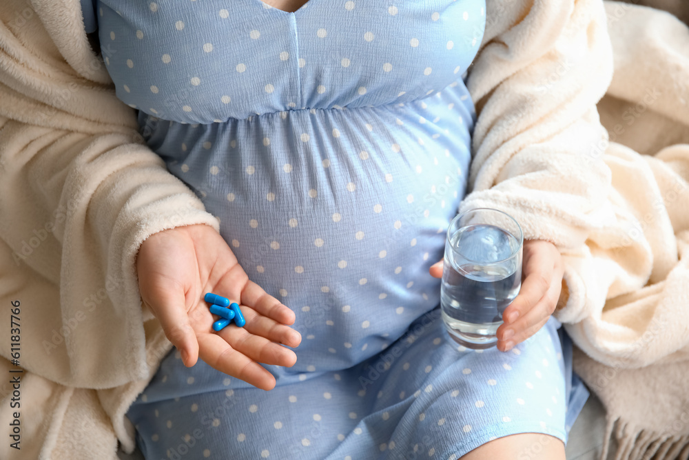 Pregnant woman with Folic Acid pills and glass of water at home, closeup