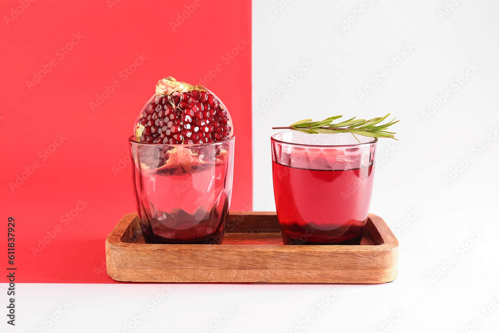 Board with glasses of fresh pomegranate juice on colorful background