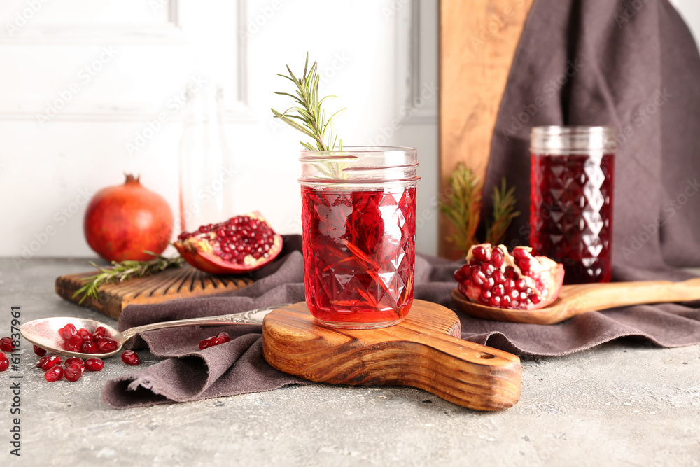 Spoon with fresh pomegranate and glasses of juice on grey table