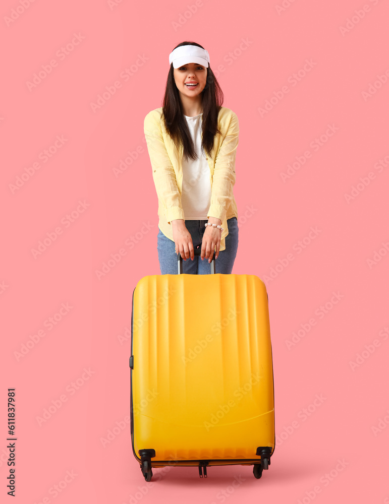 Young woman with suitcase on pink background