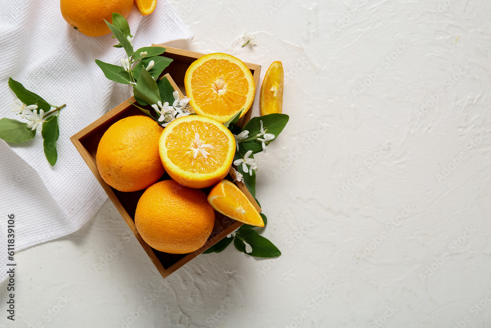 Wooden box of oranges with blooming branch on white table