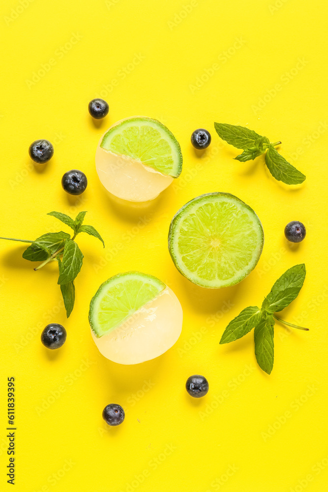 Fresh lime slices frozen in ice with blueberry and mint on yellow background