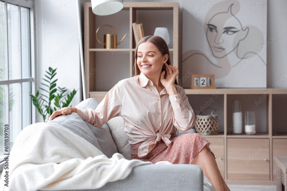 Happy young woman sitting on grey sofa in interior of light living room