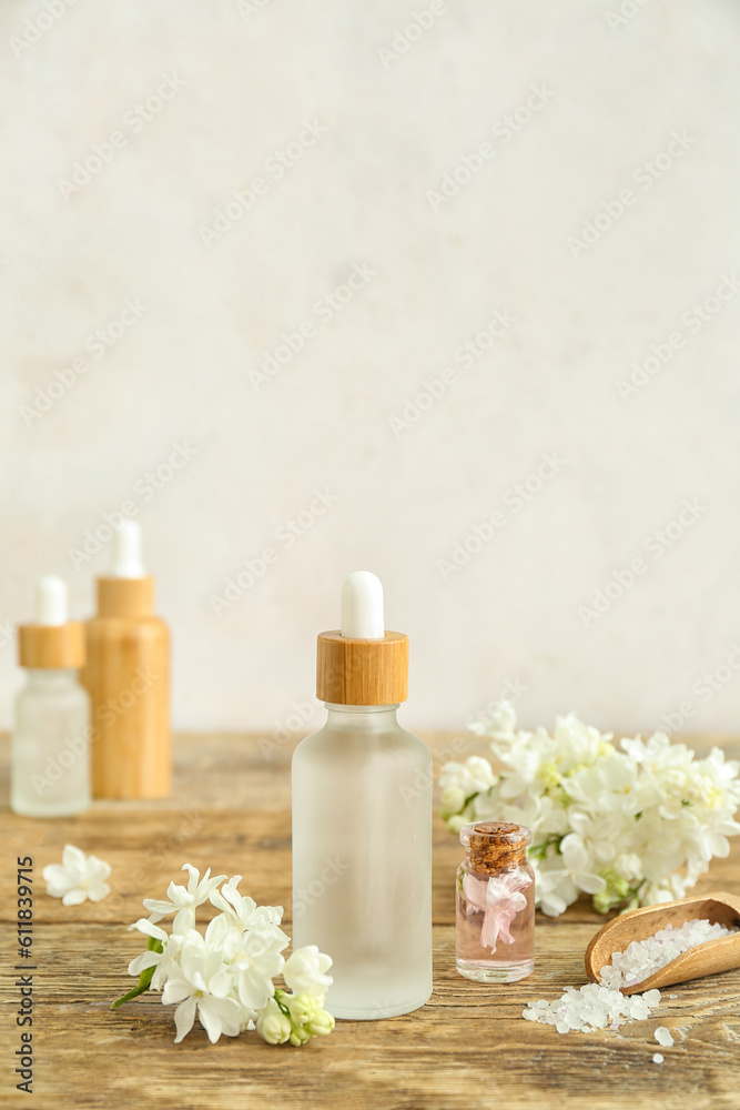 Bottles of cosmetic oil with beautiful lilac flowers and sea salt on wooden table