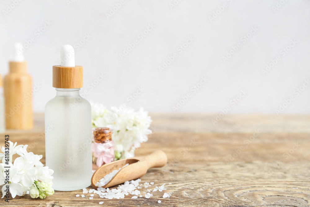 Bottles of cosmetic oil with beautiful lilac flowers and sea salt on wooden table