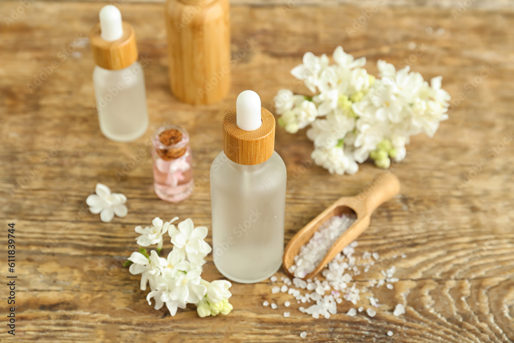 Bottles of cosmetic oil with beautiful lilac flowers and sea salt on wooden table