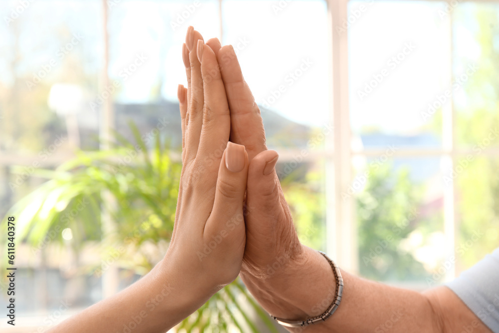 Senior woman with her granddaughter touching hands at home, closeup