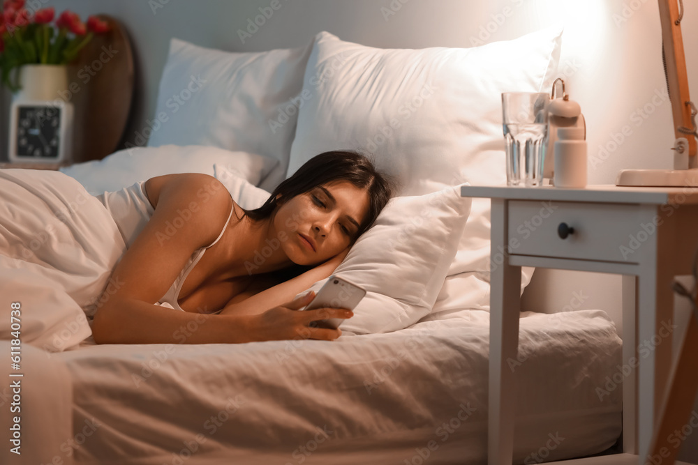 Young woman using mobile phone in bedroom at night