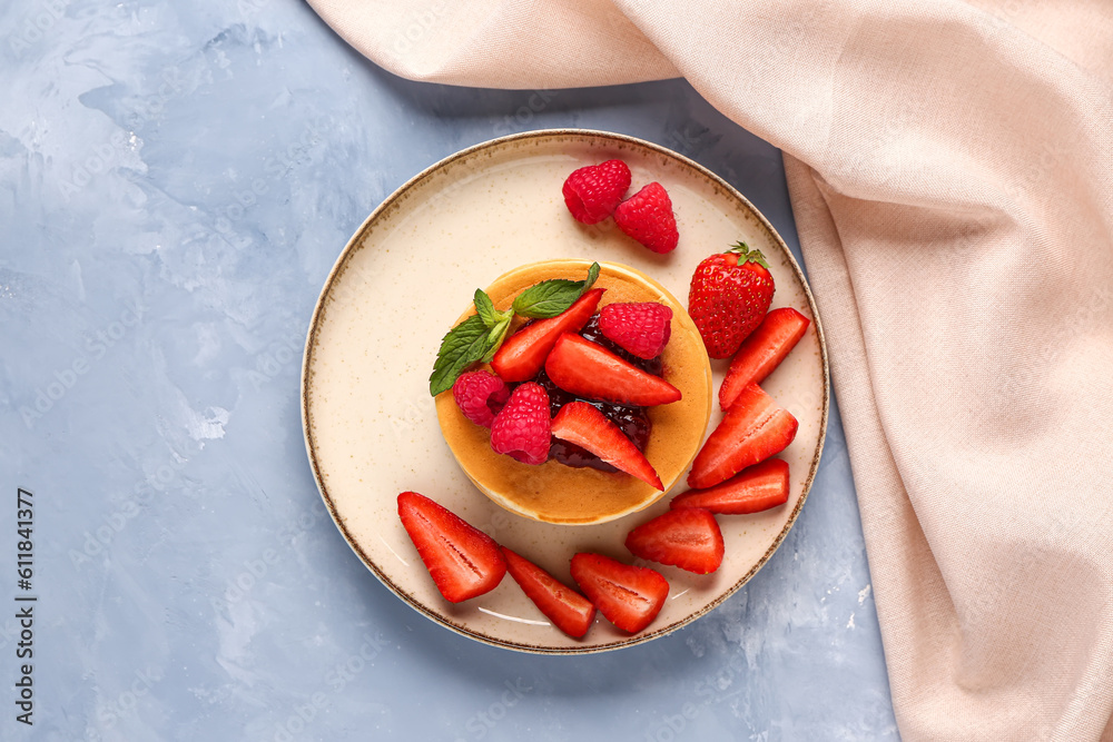 Plate with tasty pancakes and berries on blue background