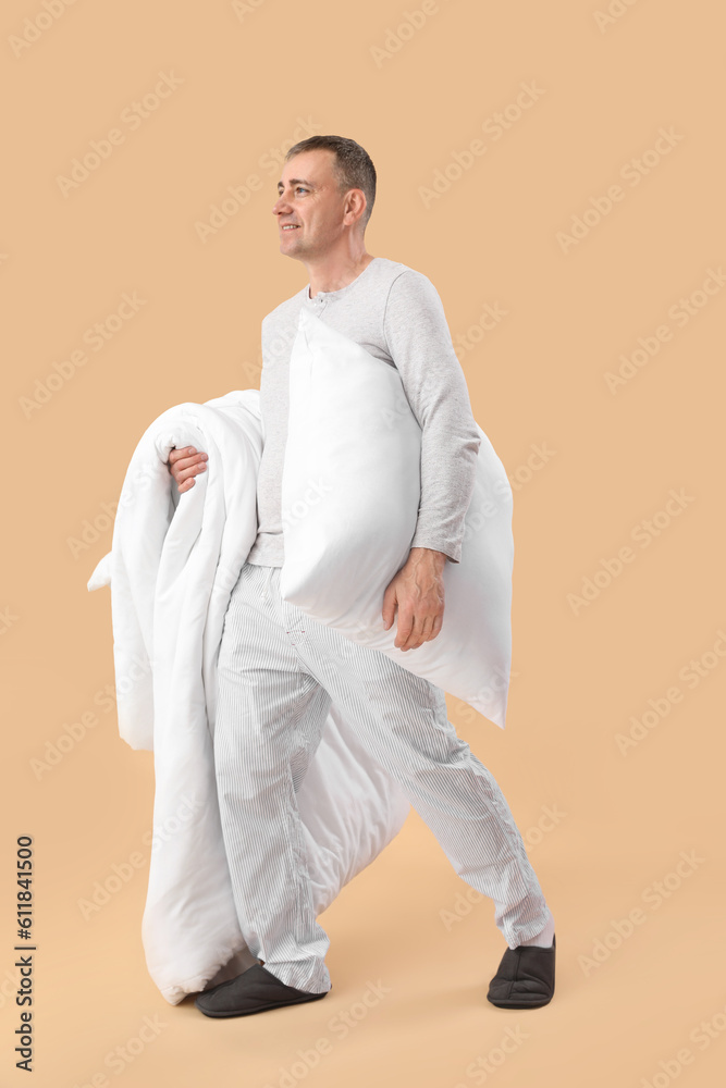 Mature man with soft pillow and blanket on beige background