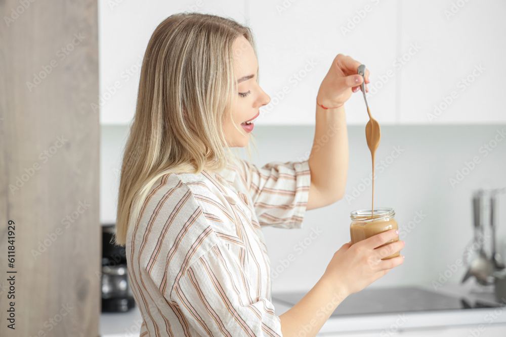 Young woman with spoon and jar of nut butter in kitchen