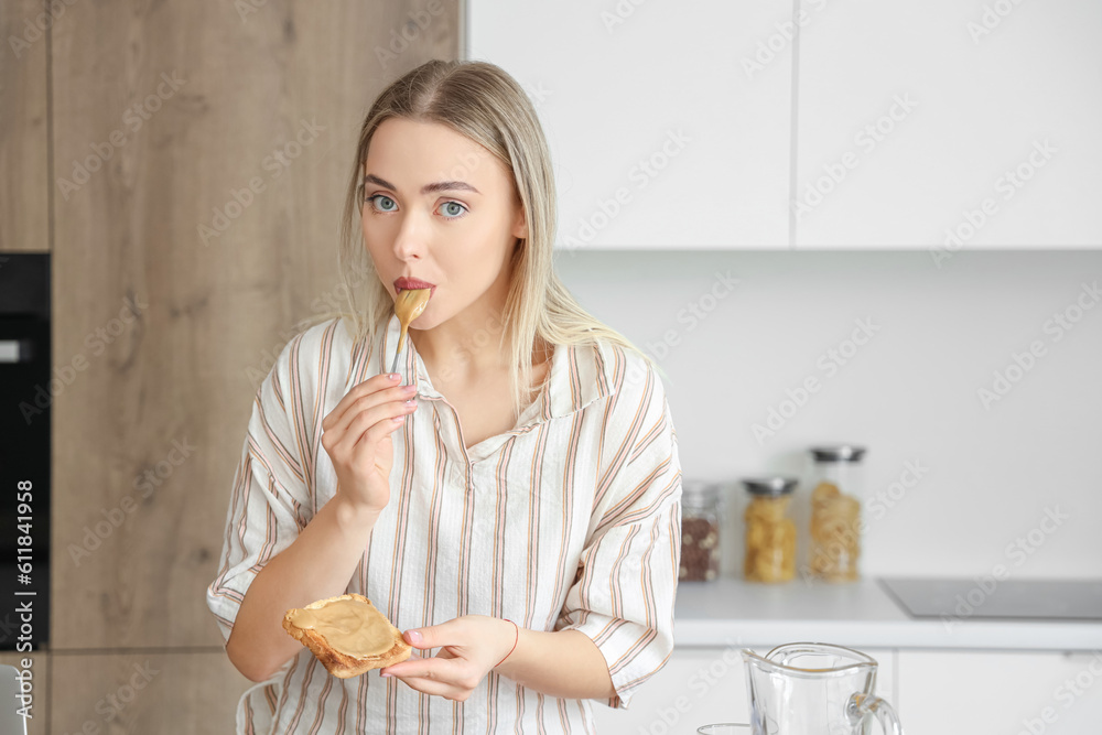 Young woman spreading tasty nut butter onto toast in kitchen