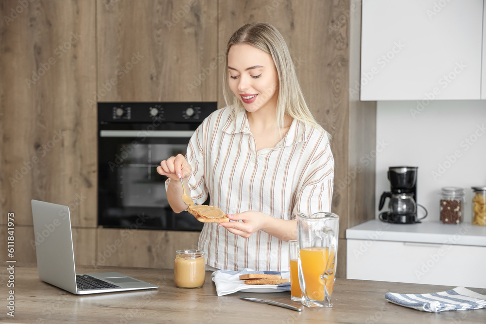 Young woman spreading tasty nut butter onto toast in kitchen