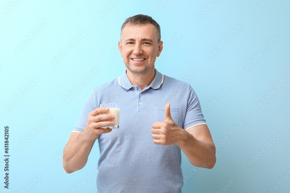 Mature man with glass of milk showing thumb-up on blue background