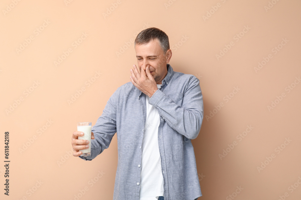 Displeased mature man with glass of milk on beige background