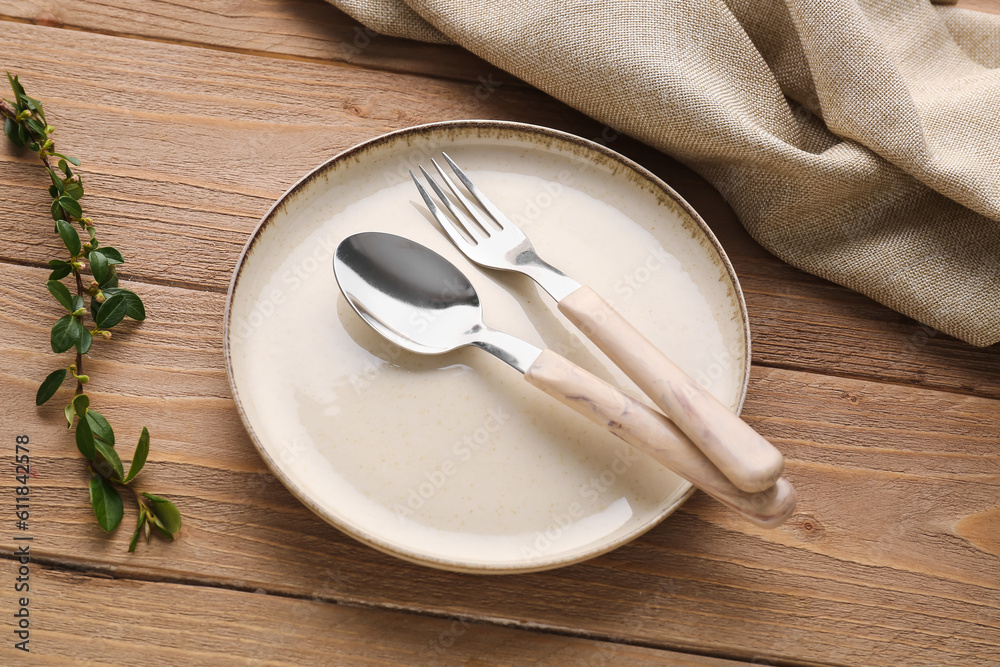 Silver spoon with fork, plate and cotoneaster twig on wooden table