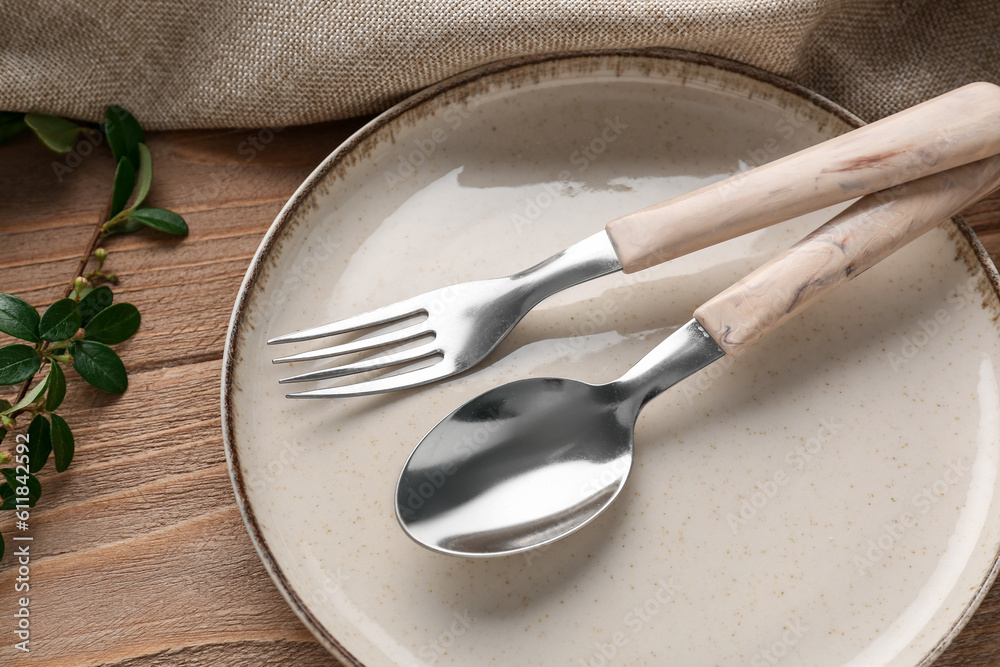 Silver spoon with fork, plate and cotoneaster twig on wooden table